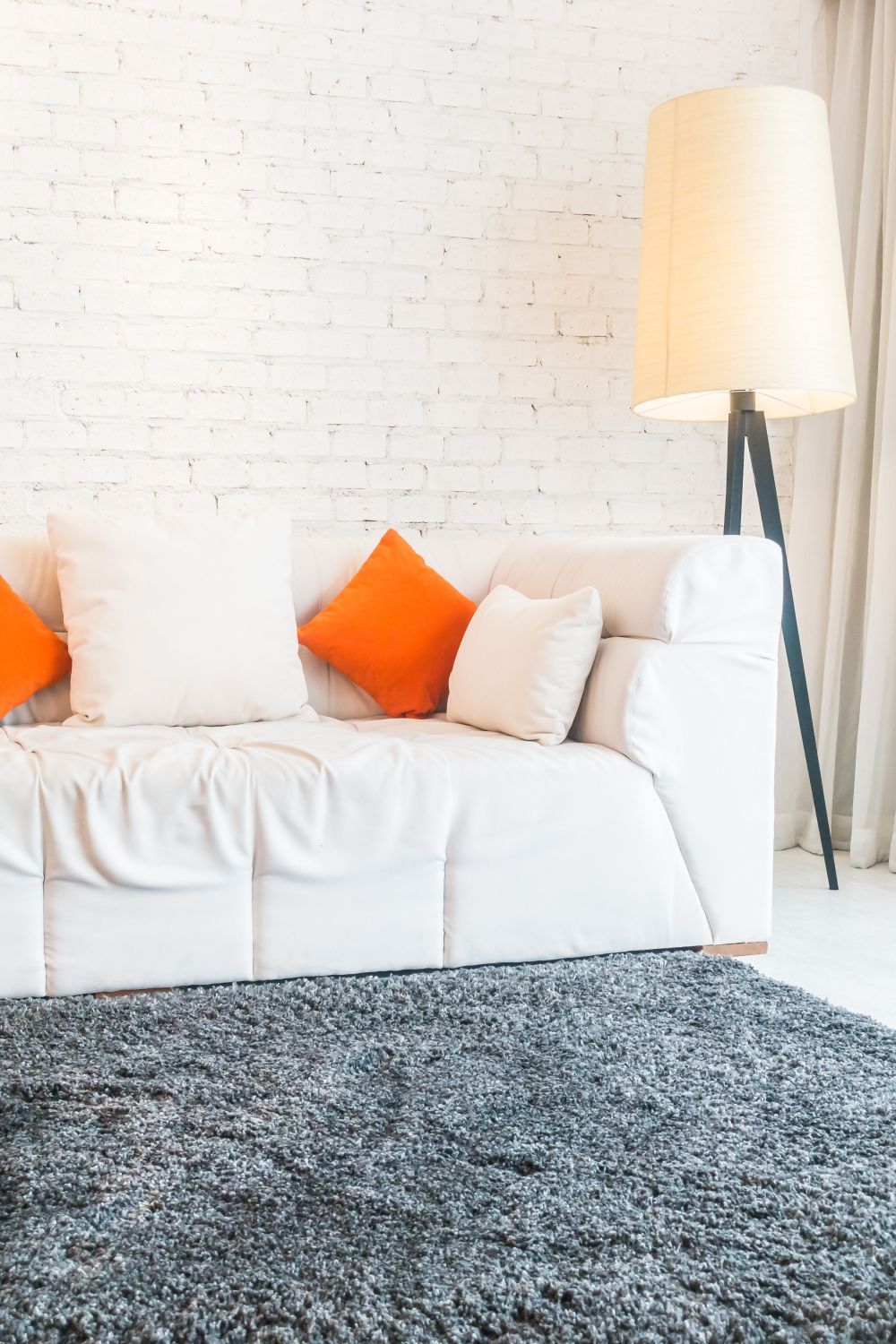 White sofa with orange throw pillows above a gray shag area rug